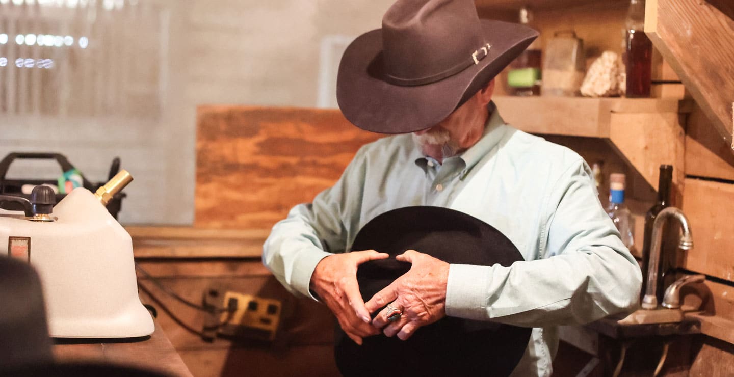 A cowboy wearing a black hat, holding and shaping a black hat.